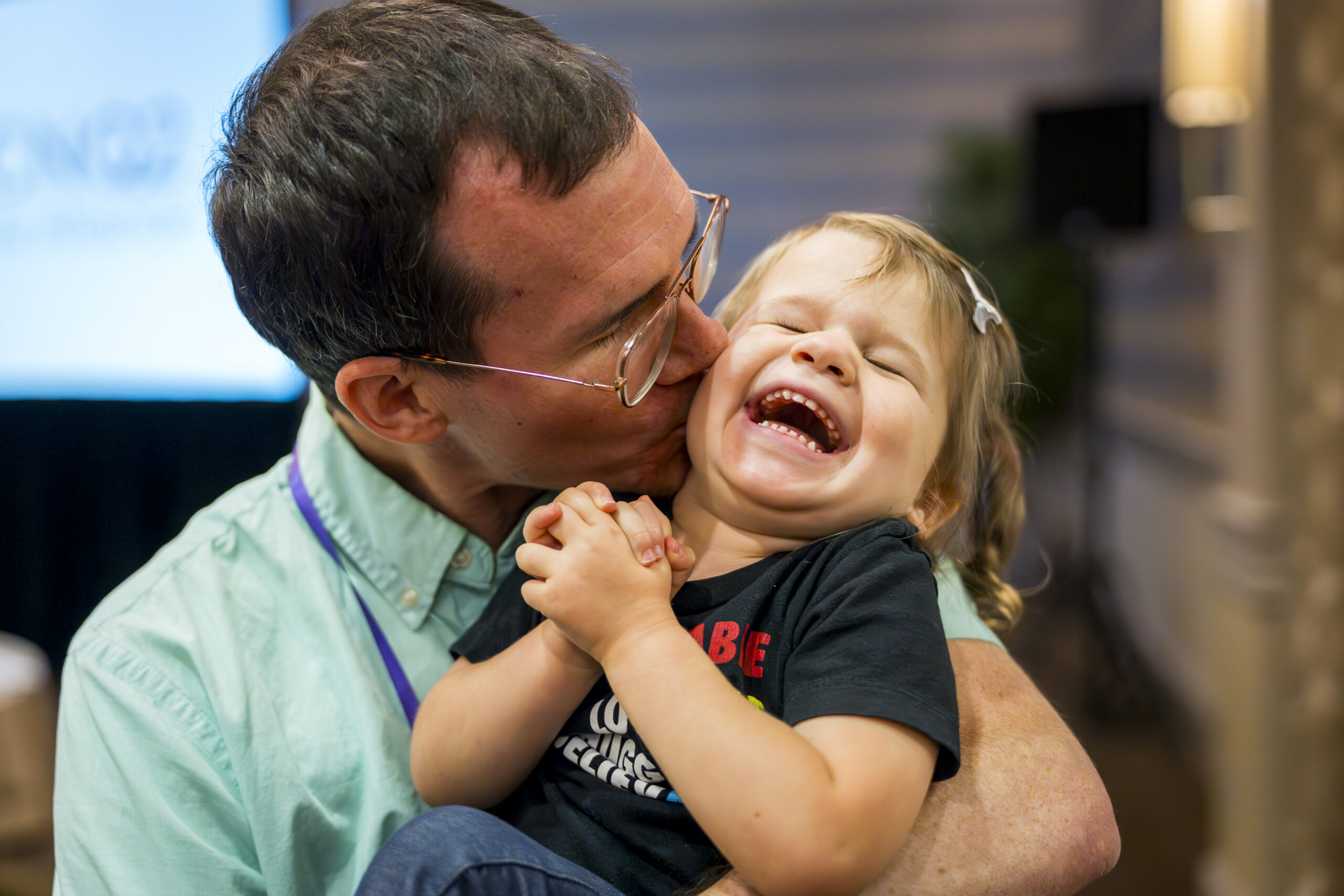 A dad kisses his laughing toddler on the cheek