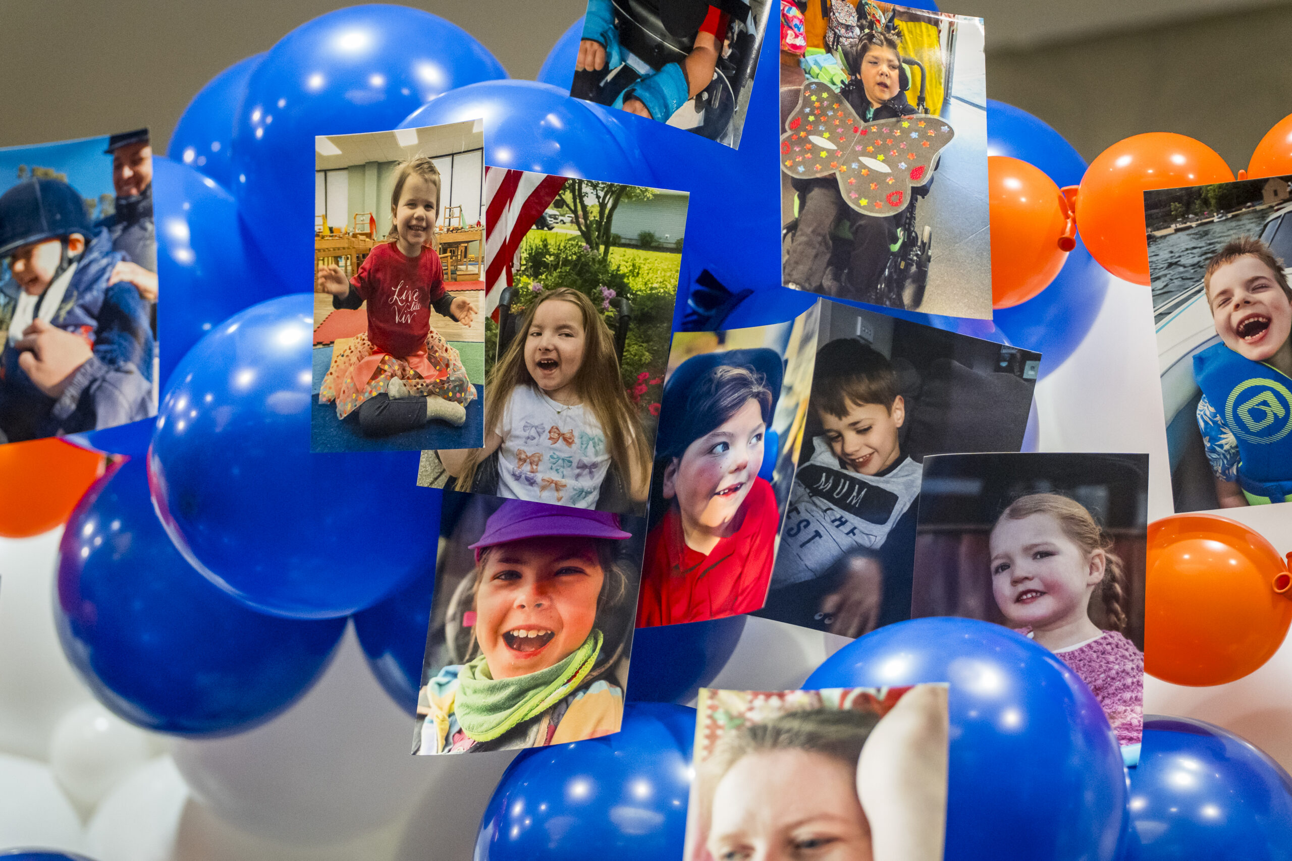 Photos of smiling KCNQ2 kiddos displayed among blue and orange balloons